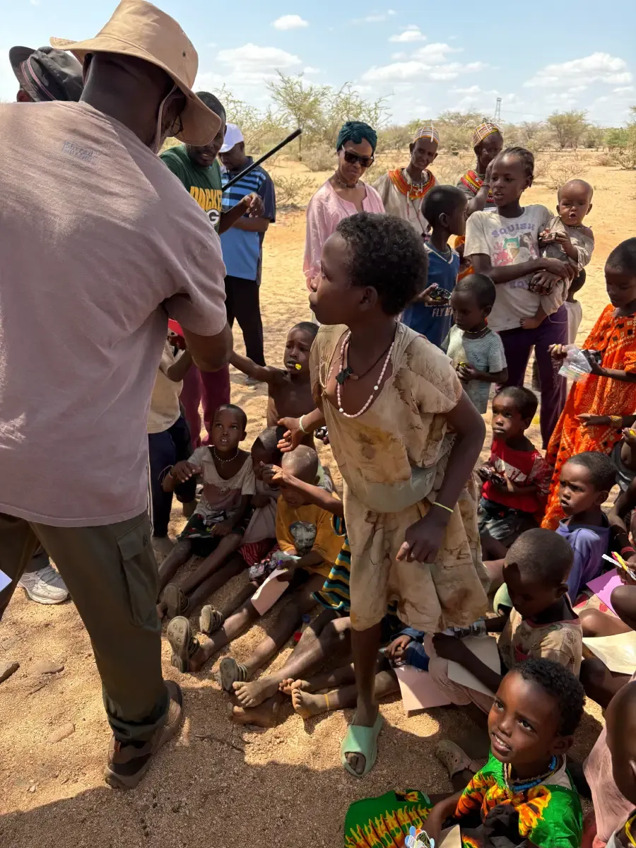A team member teaching a group of children and adults gathered outdoors in Kenya