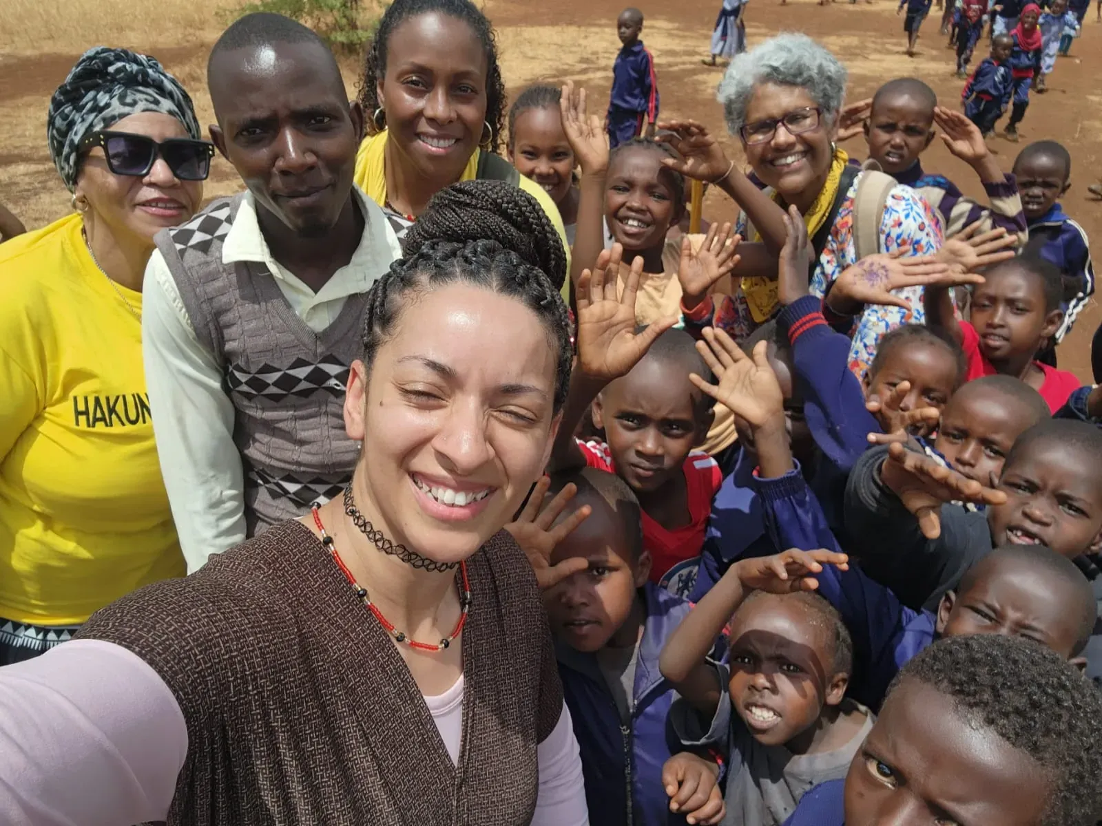 A team member surrounded by a crowd of smiling children waving at the camera