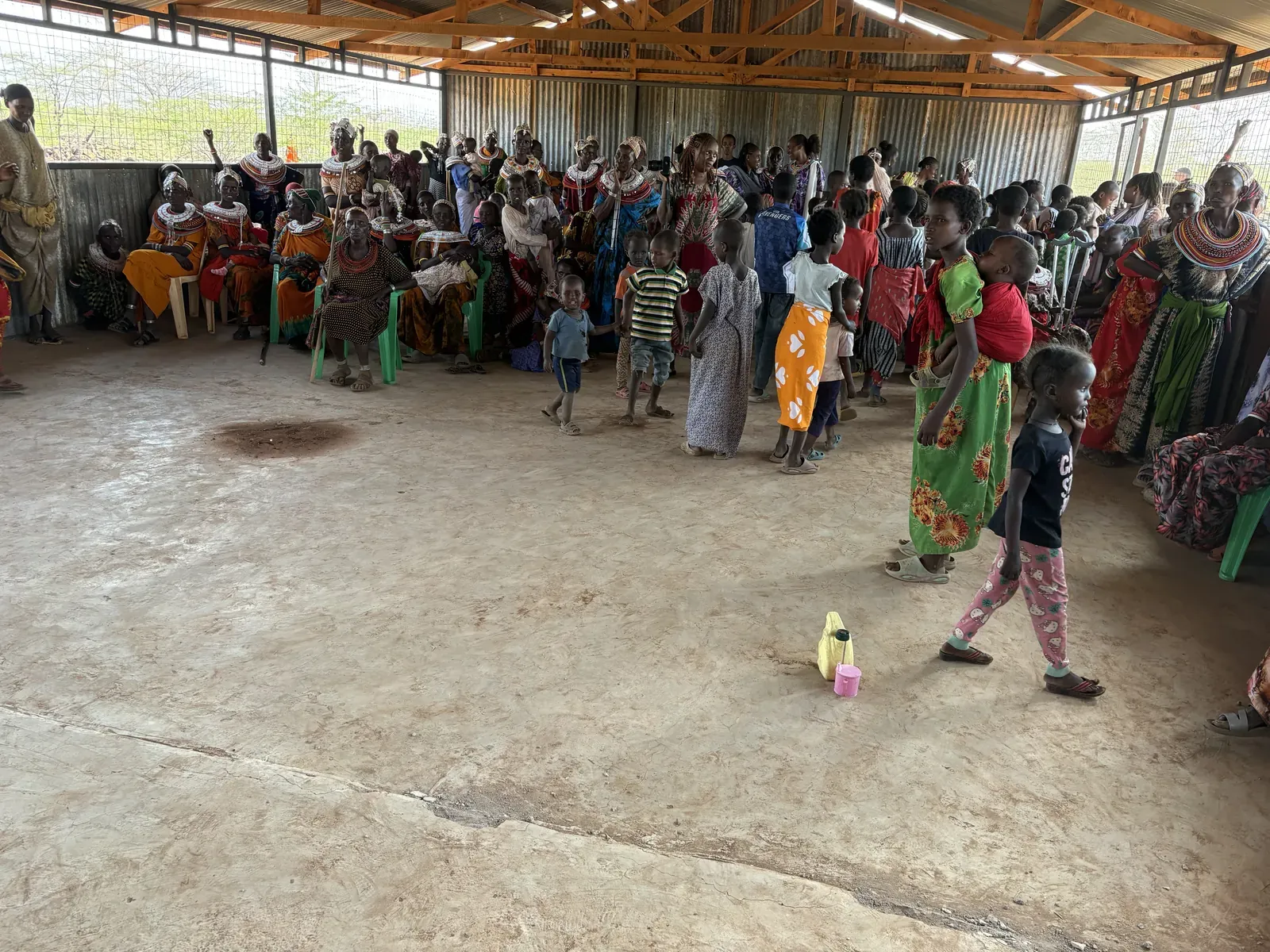 A large gathering of women and children seated and standing under a covered hall