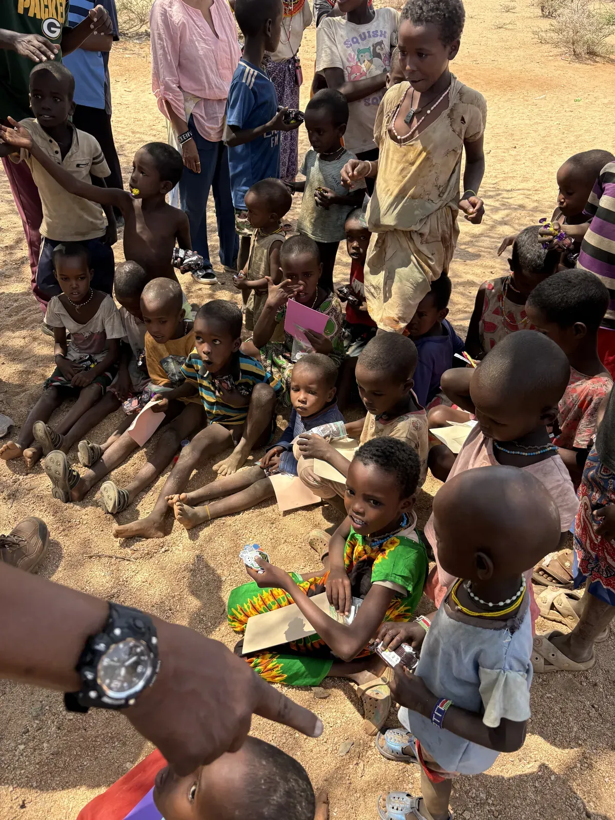 Children seated together on the ground receiving food parcels from the team